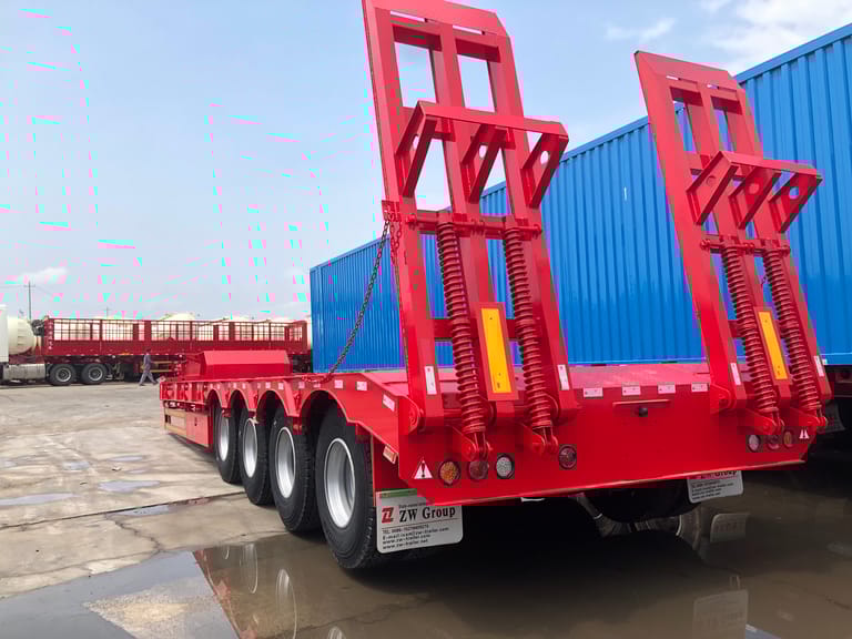 Rear three-quarter view of 100 ton lowbed semi trailer emphasizing spring-loaded ramps and durable rear frame for safe loading of heavy machinery. Rear three-quarter view of 100 ton lowbed semi trailer emphasizing spring-loaded ramps and durable rear frame for safe loading of heavy machinery.