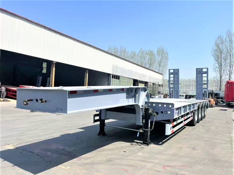Front three-quarter view of 4 axle 80 Ton Lowbed Semi Trailer highlighting low-deck design, mechanical ramps, and high-strength chassis for oversized cargo transport. Front three-quarter view of 4 axle 80 Ton Lowbed Semi Trailer highlighting low-deck design, mechanical ramps, and high-strength chassis for oversized cargo transport.