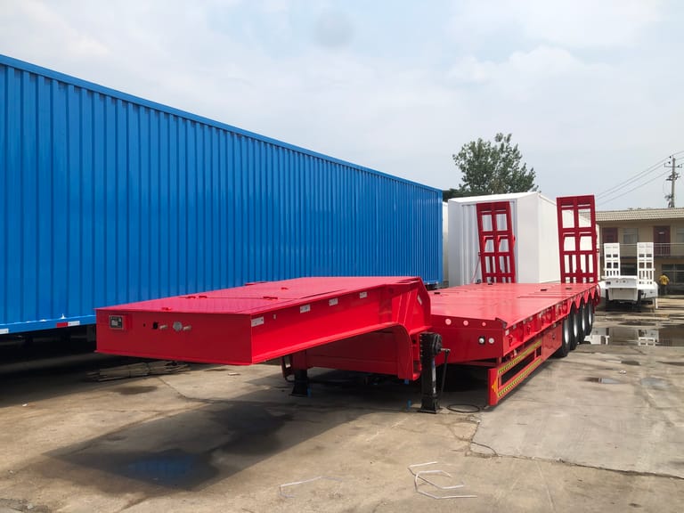 Front three-quarter view of 4 axle 100 Ton Lowbed Semi Trailer highlighting low-deck design, mechanical ramps, and high-strength chassis for oversized cargo transport. Front three-quarter view of 4 axle 100 Ton Lowbed Semi Trailer highlighting low-deck design, mechanical ramps, and high-strength chassis for oversized cargo transport.