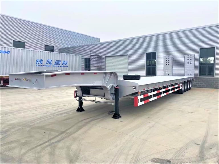 Front three-quarter view of 4 Axle 100 Ton Lowbed Semi Trailer highlighting low-deck design, mechanical suspension, and spring ramps for safe heavy equipment loading.