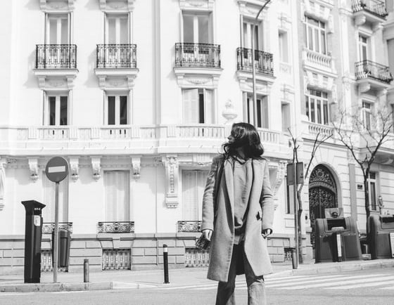 man in black coat walking on sidewalk in grayscale photography