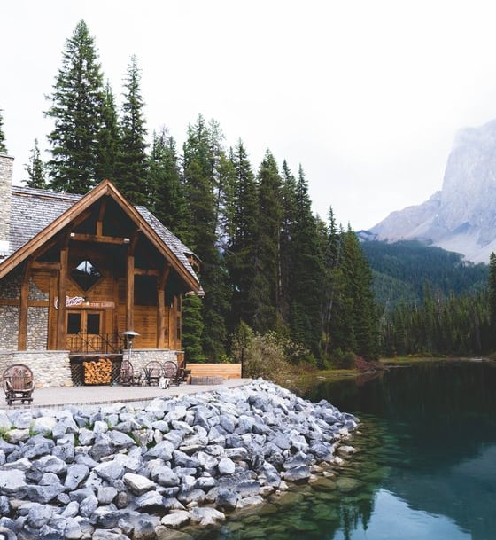 brown wooden house near lake surrounded by green trees during daytime