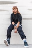 woman in black long sleeve shirt and blue denim jeans sitting on white concrete wall