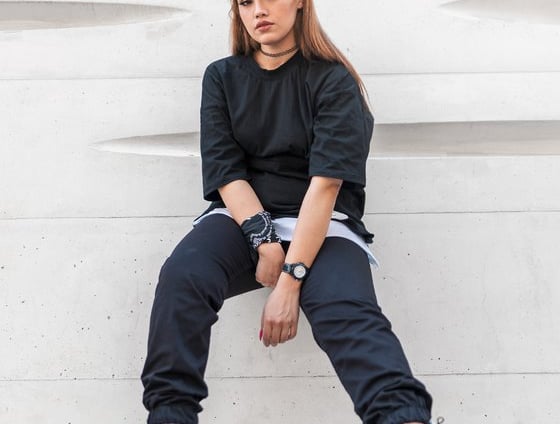 woman in black long sleeve shirt and blue denim jeans sitting on white concrete wall