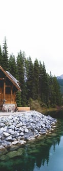 brown wooden house near lake surrounded by green trees during daytime
