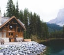 brown wooden house near lake surrounded by green trees during daytime
