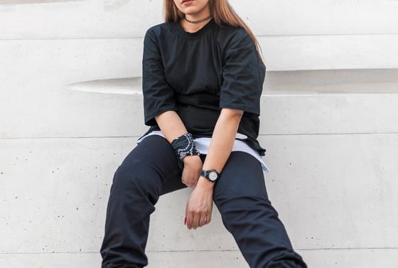 woman in black long sleeve shirt and blue denim jeans sitting on white concrete wall