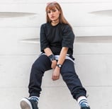 woman in black long sleeve shirt and blue denim jeans sitting on white concrete wall