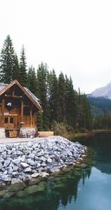 brown wooden house near lake surrounded by green trees during daytime
