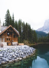 brown wooden house near lake surrounded by green trees during daytime