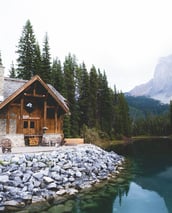 brown wooden house near lake surrounded by green trees during daytime