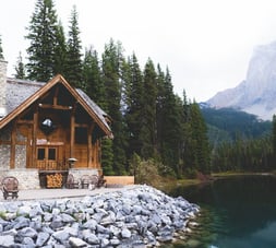 brown wooden house near lake surrounded by green trees during daytime