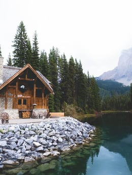 brown wooden house near lake surrounded by green trees during daytime
