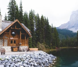 brown wooden house near lake surrounded by green trees during daytime