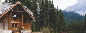 brown wooden house near lake surrounded by green trees during daytime