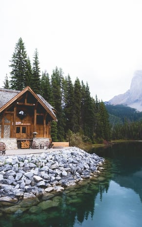 brown wooden house near lake surrounded by green trees during daytime