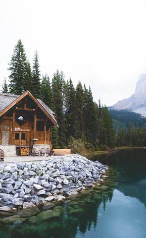 brown wooden house near lake surrounded by green trees during daytime