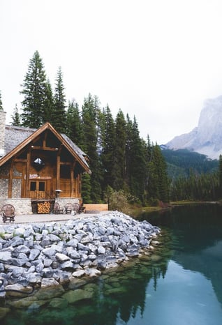 brown wooden house near lake surrounded by green trees during daytime