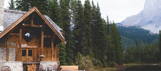brown wooden house near lake surrounded by green trees during daytime
