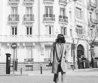 man in black coat walking on sidewalk in grayscale photography