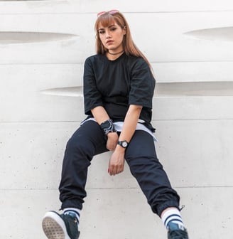 woman in black long sleeve shirt and blue denim jeans sitting on white concrete wall