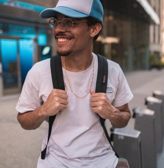 man in white crew neck t-shirt wearing blue cap and black sunglasses with back pack student