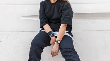 woman in black long sleeve shirt and blue denim jeans sitting on white concrete wall