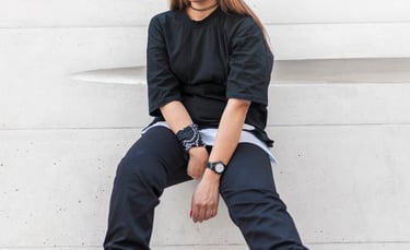 woman in black long sleeve shirt and blue denim jeans sitting on white concrete wall