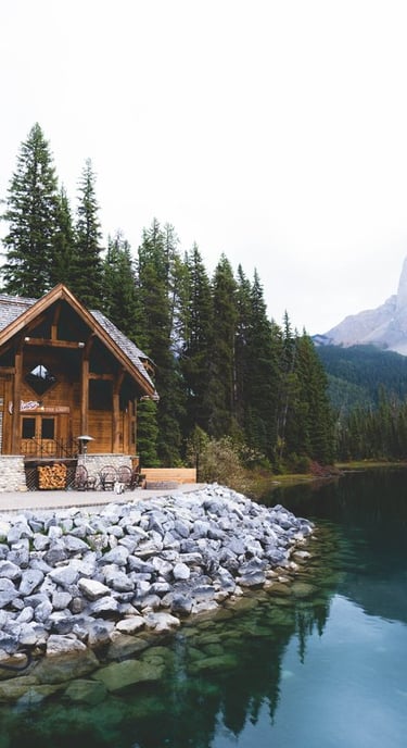 brown wooden house near lake surrounded by green trees during daytime