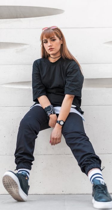 woman in black long sleeve shirt and blue denim jeans sitting on white concrete wall