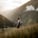 man in gray jacket and black backpack standing on green grass field near mountain during daytime