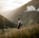 man in gray jacket and black backpack standing on green grass field near mountain during daytime