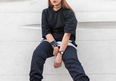 woman in black long sleeve shirt and blue denim jeans sitting on white concrete wall