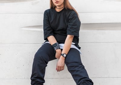 woman in black long sleeve shirt and blue denim jeans sitting on white concrete wall