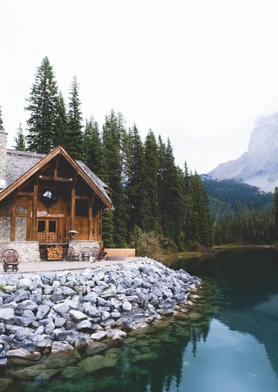 brown wooden house near lake surrounded by green trees during daytime