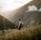 man in gray jacket and black backpack standing on green grass field near mountain during daytime