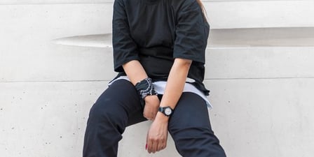 woman in black long sleeve shirt and blue denim jeans sitting on white concrete wall