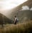 man in gray jacket and black backpack standing on green grass field near mountain during daytime