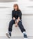woman in black long sleeve shirt and blue denim jeans sitting on white concrete wall