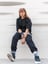 woman in black long sleeve shirt and blue denim jeans sitting on white concrete wall