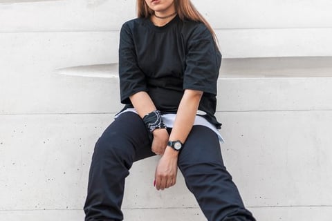 woman in black long sleeve shirt and blue denim jeans sitting on white concrete wall