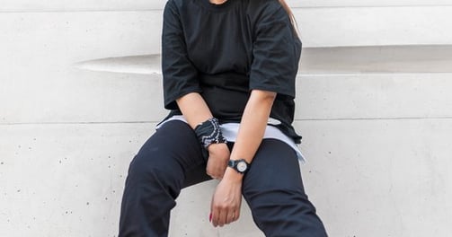 woman in black long sleeve shirt and blue denim jeans sitting on white concrete wall