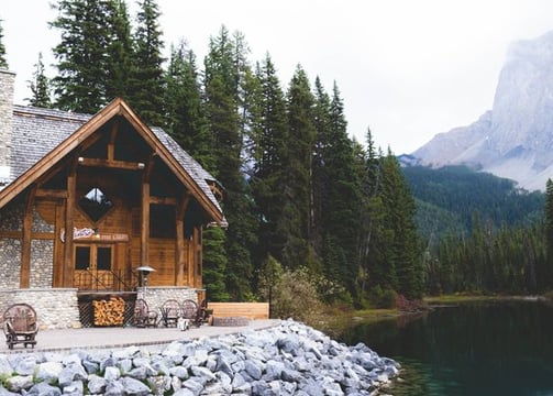 brown wooden house near lake surrounded by green trees during daytime