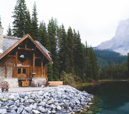 brown wooden house near lake surrounded by green trees during daytime