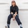 woman in black long sleeve shirt and blue denim jeans sitting on white concrete wall