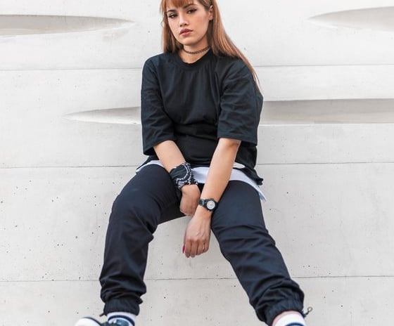 woman in black long sleeve shirt and blue denim jeans sitting on white concrete wall