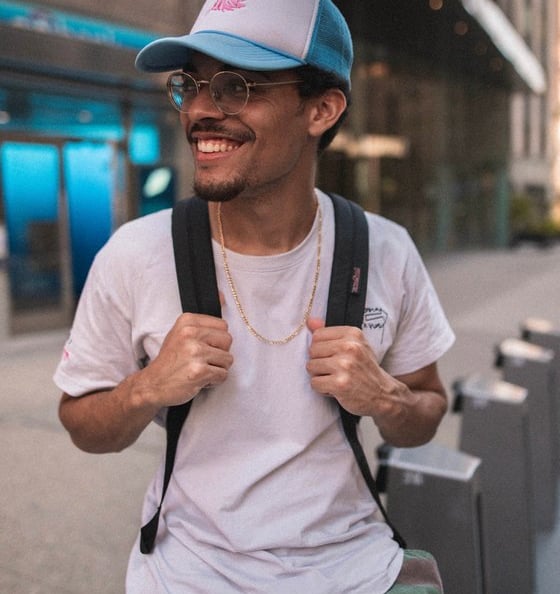man in white crew neck t-shirt wearing blue cap and black sunglasses with back pack student