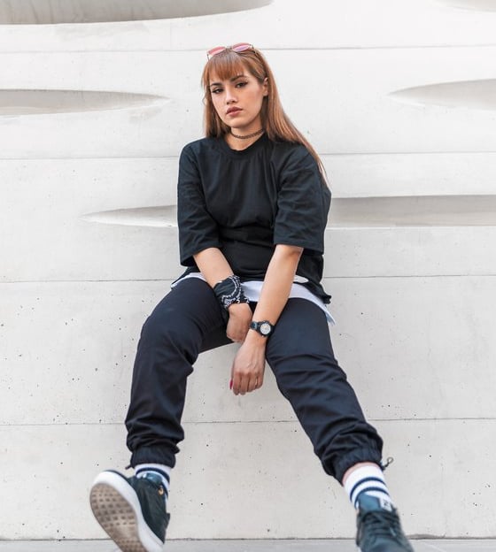 woman in black long sleeve shirt and blue denim jeans sitting on white concrete wall