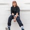 woman in black long sleeve shirt and blue denim jeans sitting on white concrete wall