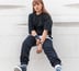 woman in black long sleeve shirt and blue denim jeans sitting on white concrete wall